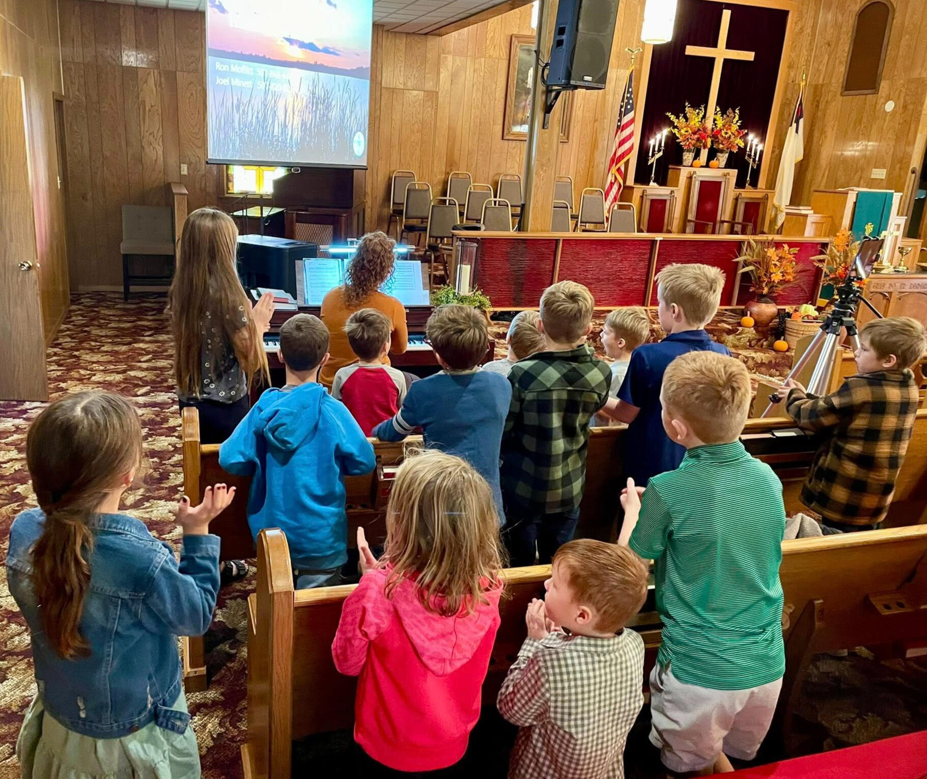 Sunday School children and teachers gathering around the piano to sing